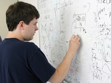A young male summer student at DESY writing mathematical formulas on a whiteboard