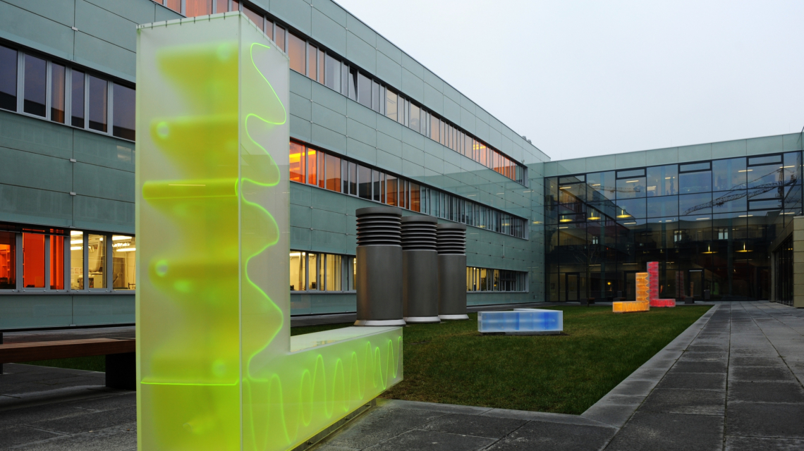 Blick in den Innenhof der Mathematisch-Naturwissenschaftlichen Fakultät der Universität Potsdam. Im Vordergrund ein L-Förmiges  neongelbes Kunstobjekt mit wellenförmiger Innenstruktur.